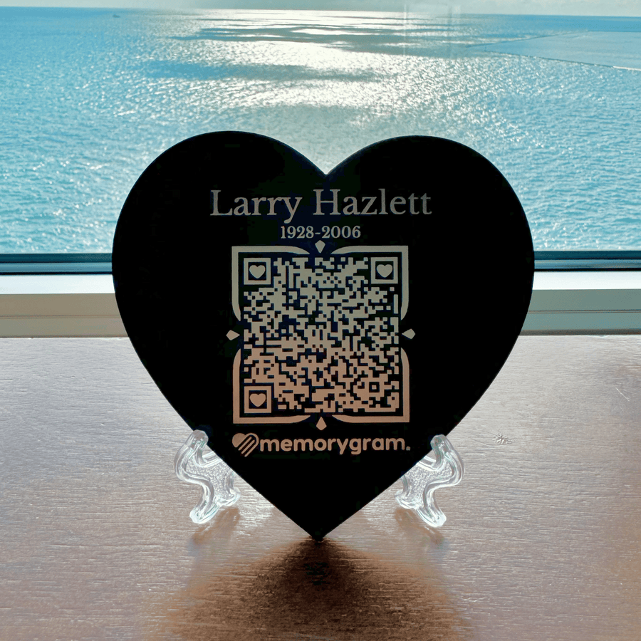 Black heart Memorygram QR medallion engraved with Larry Hazlett 1928-2006, on its stand by the water