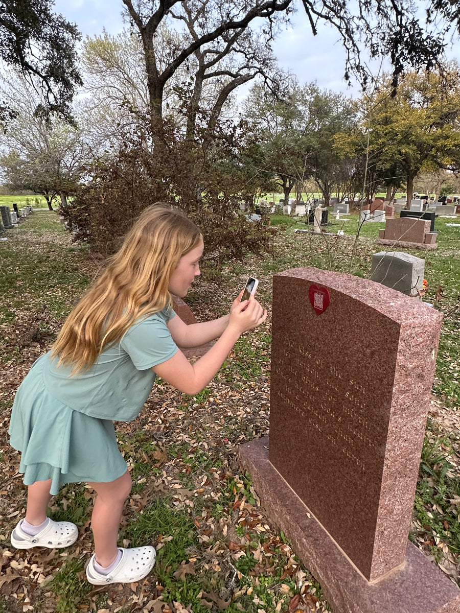 A girl scans the medallion on her family headstone with a phone